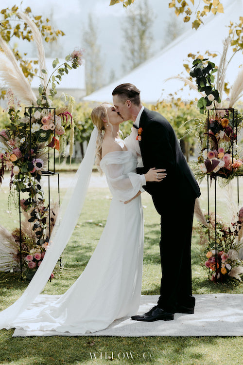 Wedding couple sharing a first kiss under a beautiful floral wedding arbour created by mudgee monkey florist